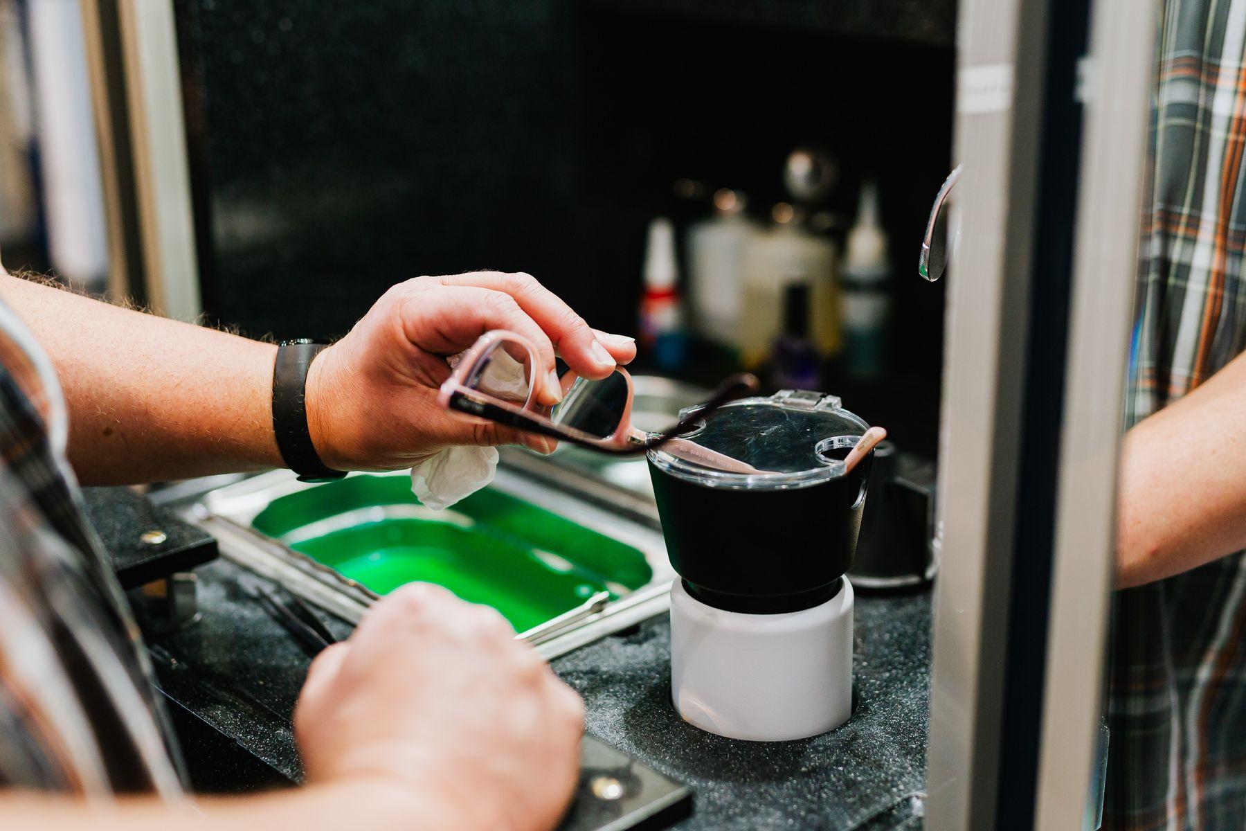 Hands cleaning a pair of glasses at an optician's workbench