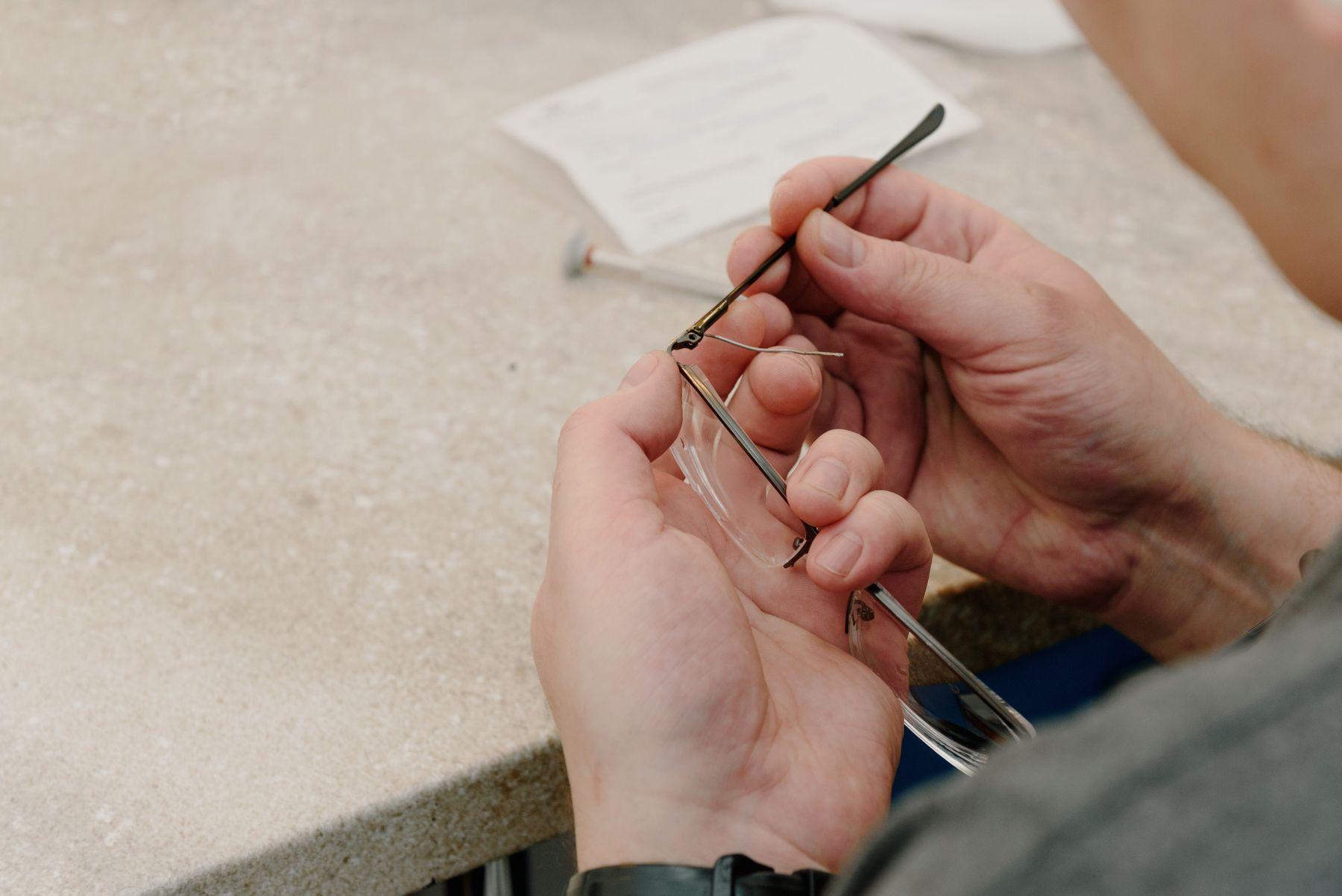 A craftsman fastening the temple of a pair of glasses with a tiny screwdriver