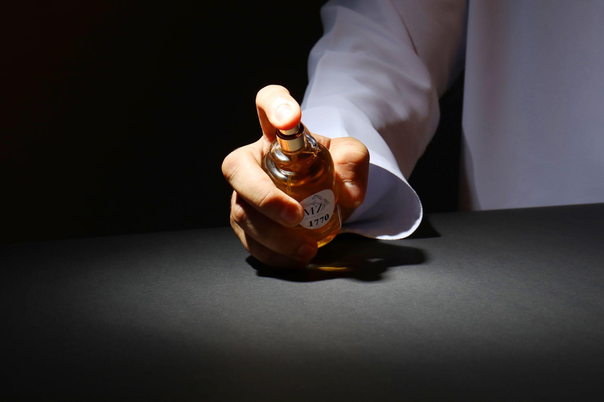 A hand holding the flacon under a single spotlight