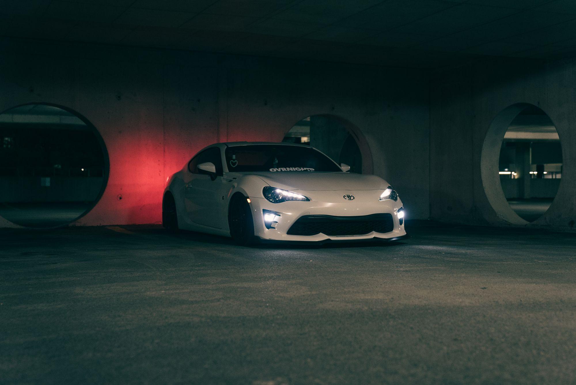 The Castellane GT in pearl white, headlights on, in a concrete garage