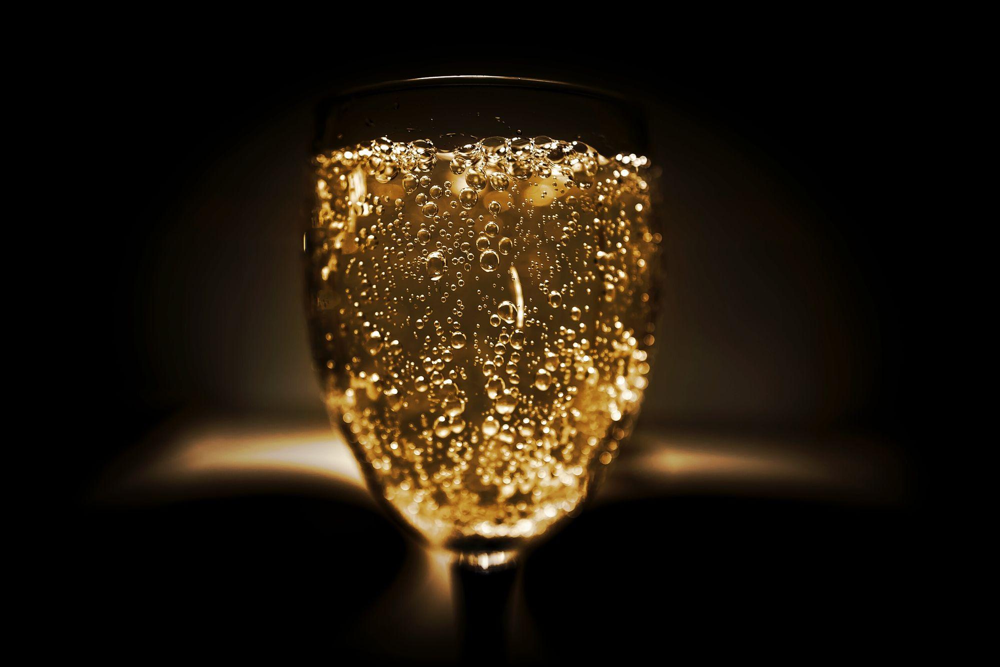 A glass of champagne glowing gold, dense with bubbles